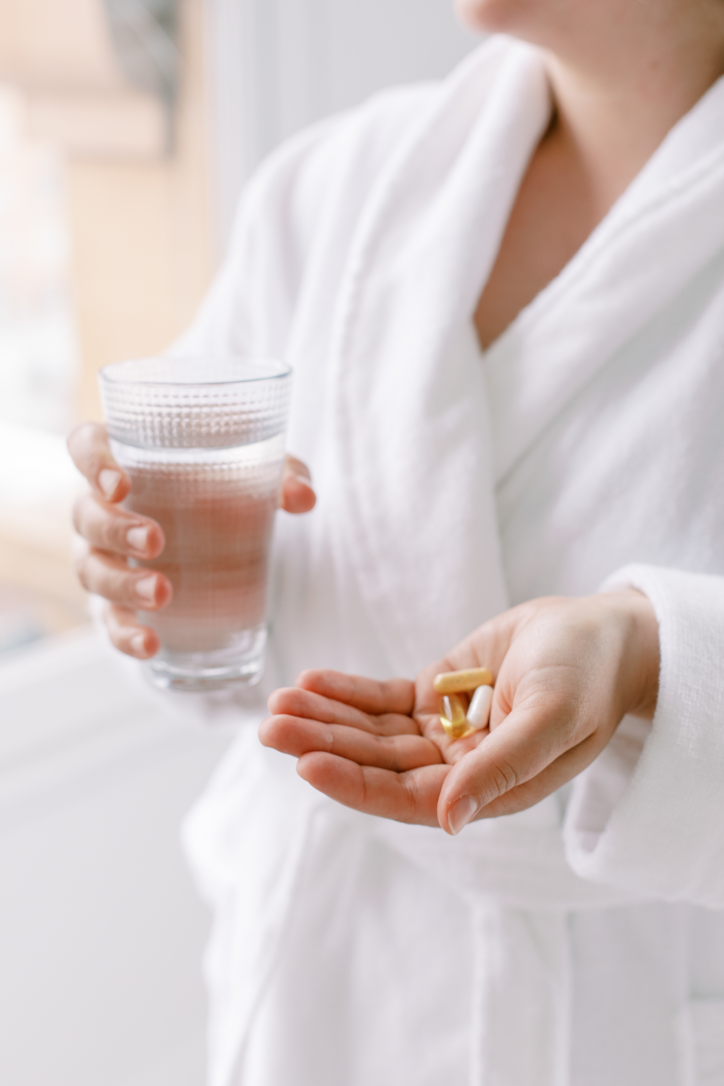 White woman in white robe holding a glass of water and supplements