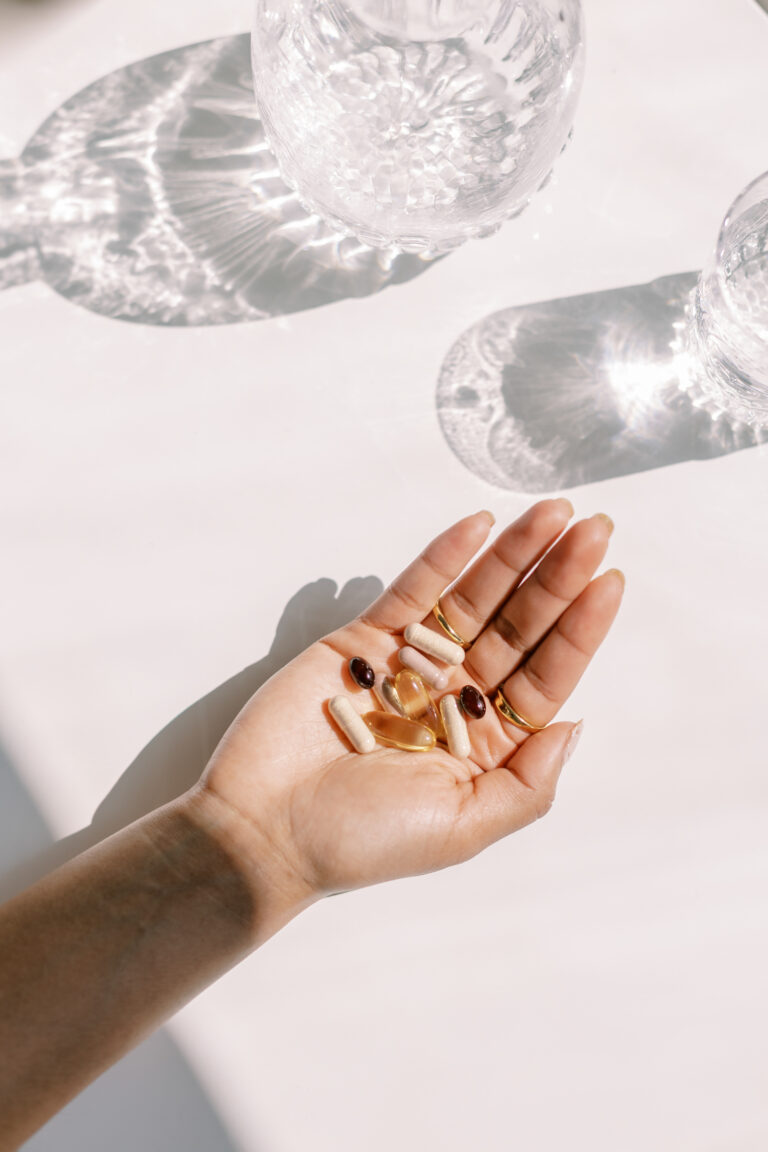 hand holding vitamin supplements next to clear classes of water