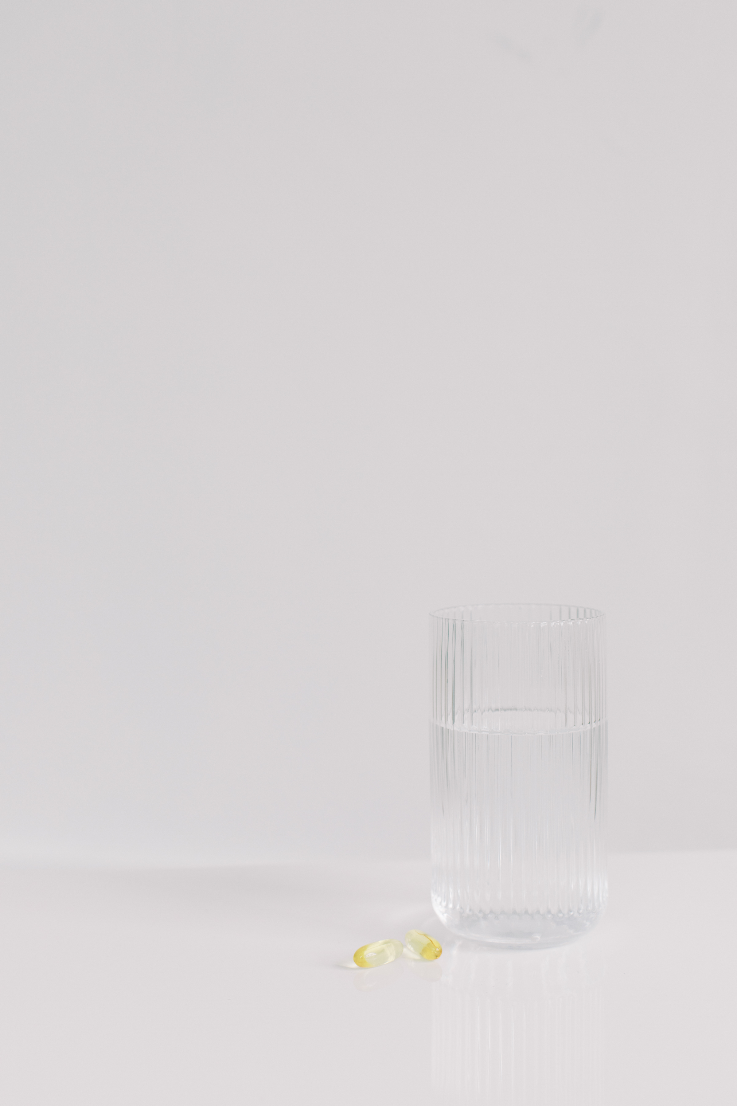 Tall glass of water with a supplement tablet against a white surface