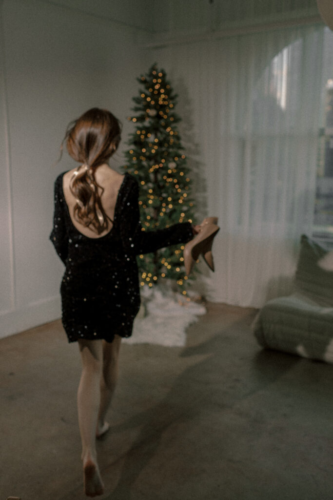 Back of young brunette woman in a black dress in a room with a christmas tree