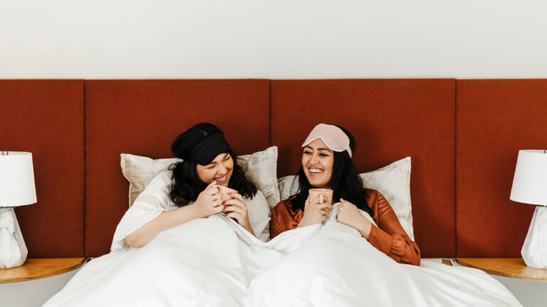 Best friends laughing in bed drinking coffee