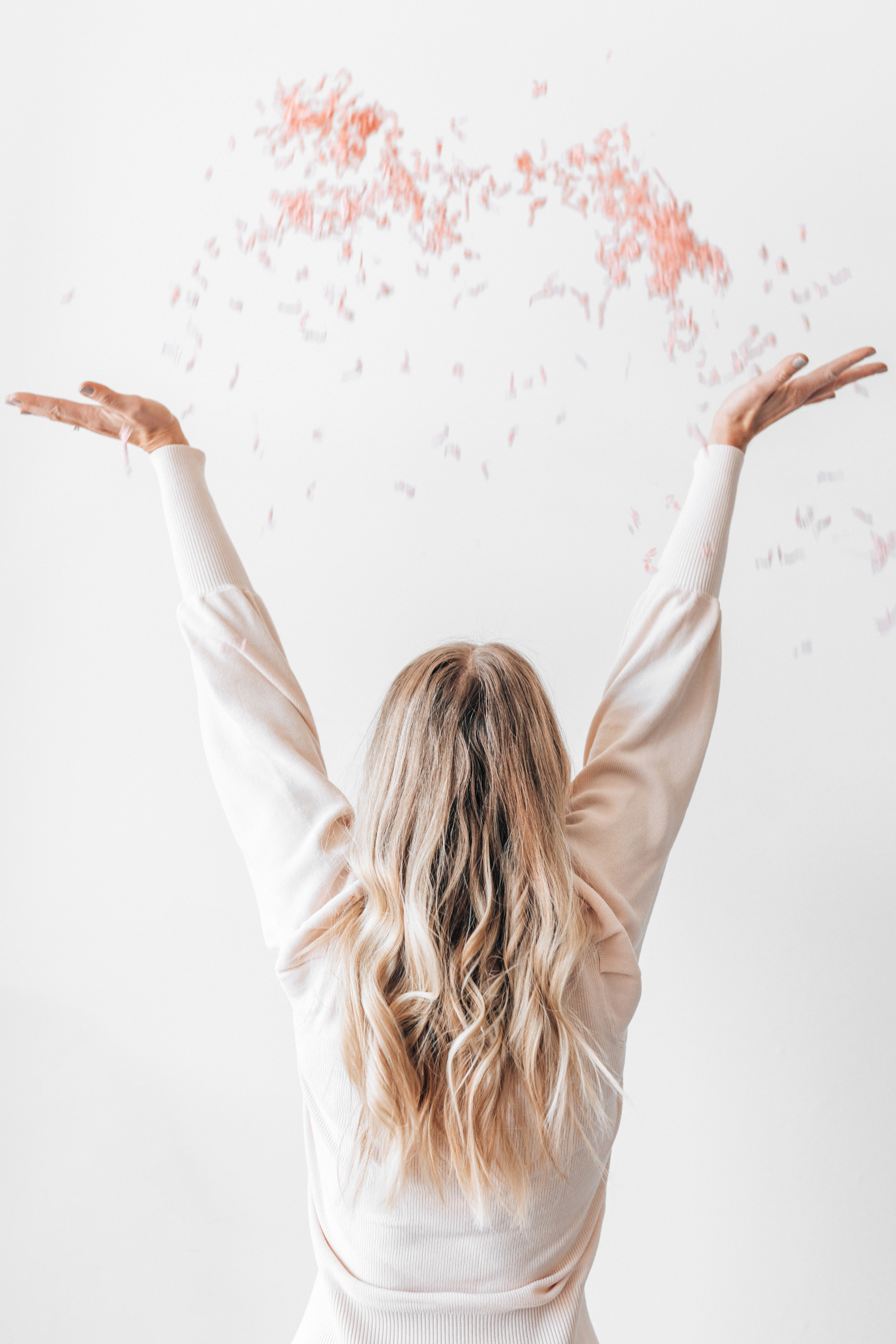 back of a slim blonde woman throwing pink confetti into the air