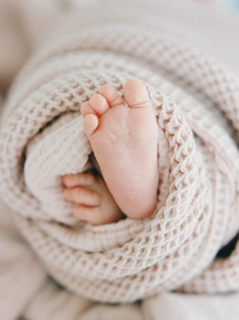 White newborn baby feet wrapped in a neutral blanket