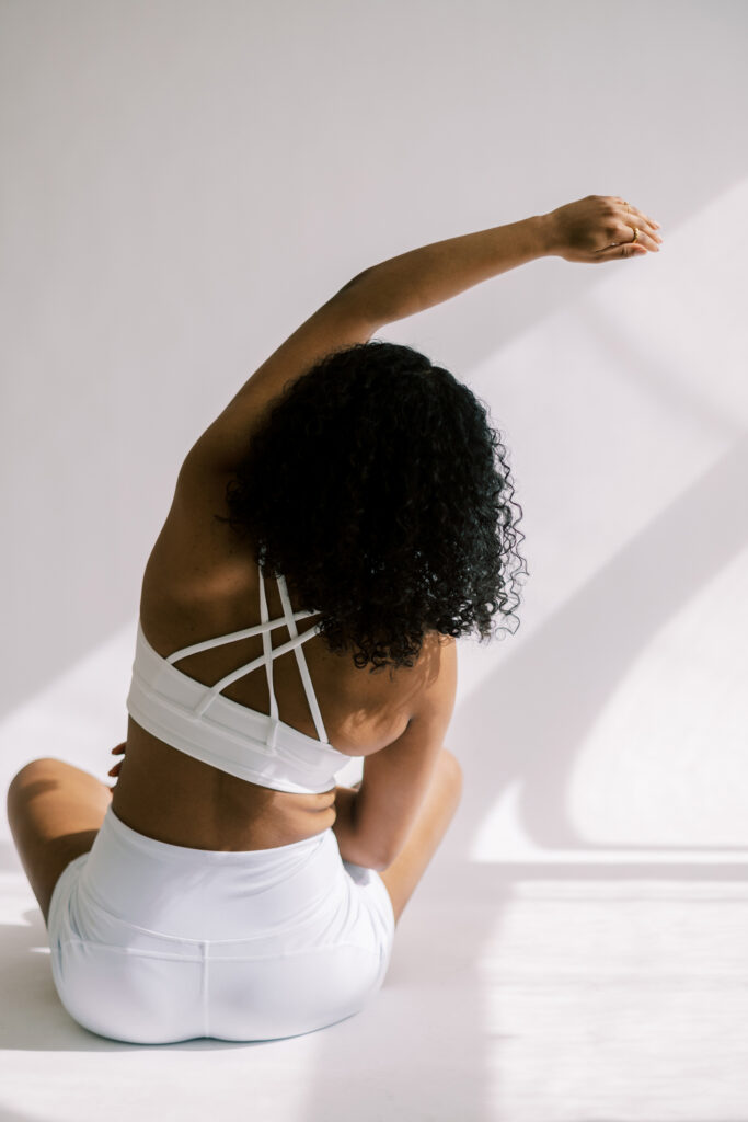 Beautiful black woman dressed in white workout gear facing the wall stretching arm out