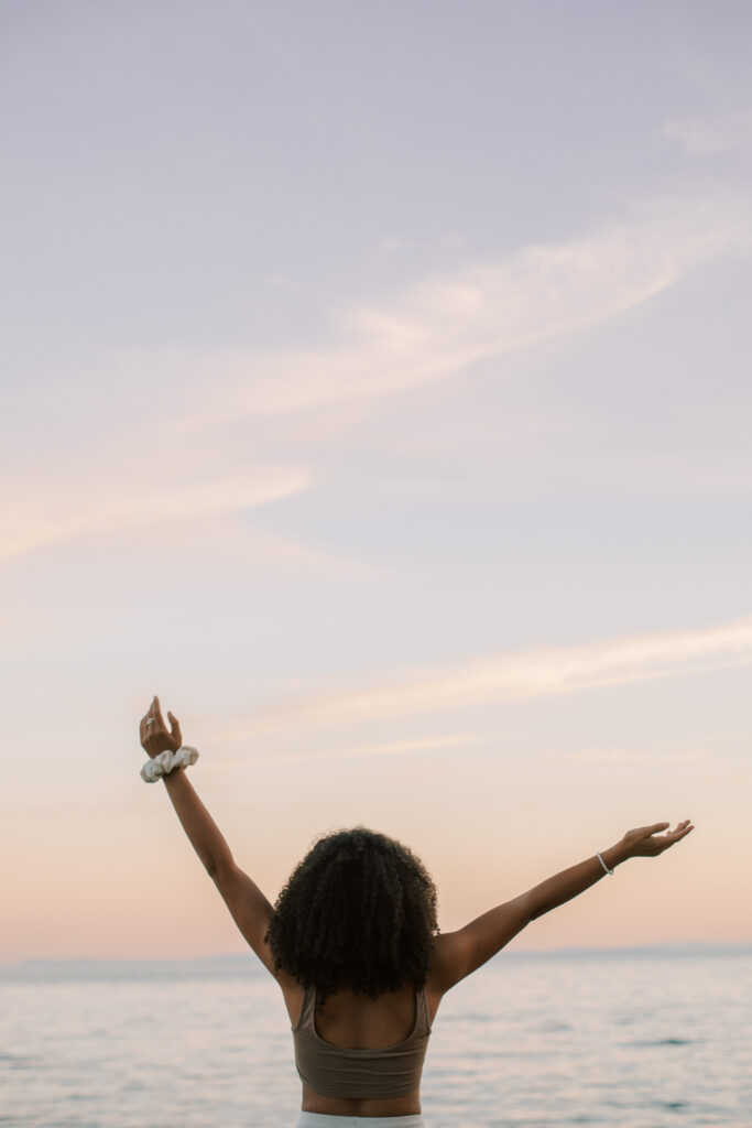 Beautiful black woman facing the ocean with hands in the air