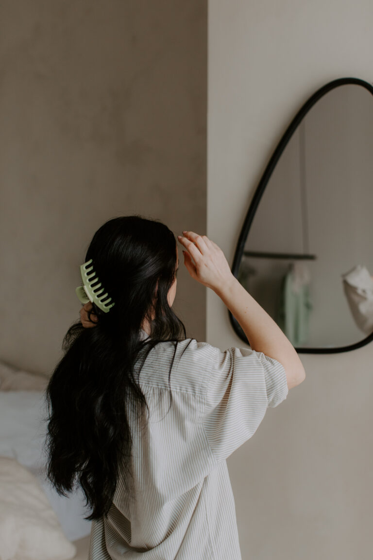 Young woman with long dark hair wearing white shirt looking in a mirror